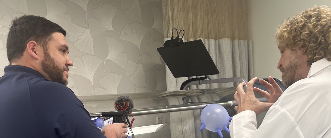 Joseph Dituri explaining molecular models beside a hyperbaric chamber while being filmed